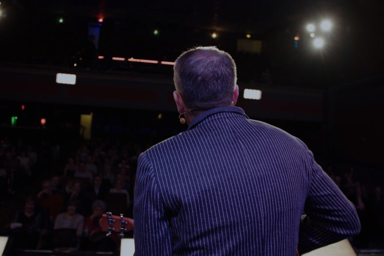 Rob Skinner with his back to the camera singing to the audience